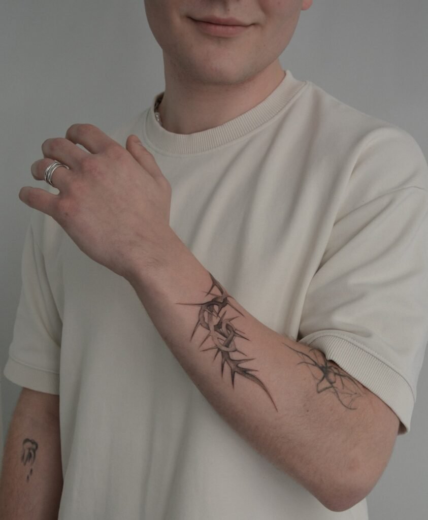 Wyrazisty tatuaż fine line z abstrakcyjną, kolczastą kompozycją o ostrych, dynamicznych formach, umieszczony na przedramieniu. Wykonany czarnym tuszem z precyzyjną kreską i subtelnym cieniowaniem, ten ekspresyjny projekt łączy siłę, strukturę i nowoczesną symbolikę w czystym, współczesnym stylu. Tatuaż wykonany przez Sonyę (@inksefer) w Fineline Tattoo Gallery dla Tattoo Kraków Kolektyw Artystów.