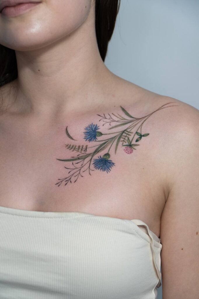 Delikatny, kolorowy tatuaż florystyczny umieszczony na obojczyku, przedstawiający fine line chabry oraz subtelne botaniczne gałązki. Lekka, kobieca i naturalna kompozycja, zaprojektowana z myślą o osobach poszukujących eleganckiego, organicznego motywu kwiatowego. Tatuaż wykonany przez Olgę Sankovą (@olga_sankova_tattoo) w Fineline Tattoo Gallery dla Tattoo Kraków Kolektyw Artystów.