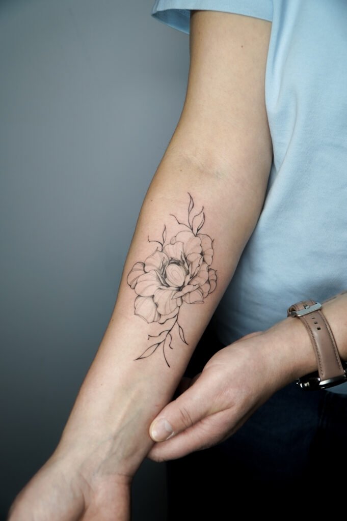 Tatuaż fine line z konturowym motywem kwiatu, umieszczony na przedramieniu, wykonany w szkicowej technice linework. Czysta, precyzyjna kompozycja botaniczna o rysunkowym, odręcznym charakterze, stworzona z myślą o miłośnikach minimalistycznych tatuaży kwiatowych. Tatuaż wykonany przez Olgę Sankovą (@olga_sankova_tattoo) w Fineline Tattoo Gallery dla Tattoo Kraków Kolektyw Artystów.