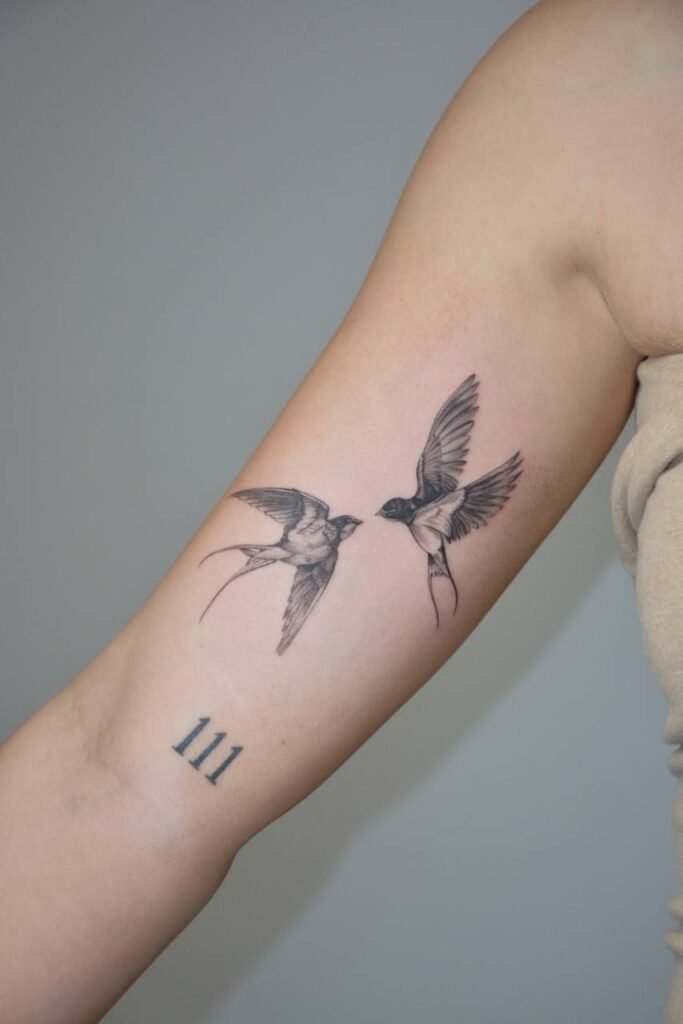 Delikatny tatuaż fine line przedstawiający dwie jaskółki w locie, umieszczony na przedramieniu. Subtelna, symboliczna kompozycja wyrażająca wolność, miłość oraz ideę powrotu do domu, podkreślona precyzyjnym, miękkim cieniowaniem. Tatuaż wykonany przez Olgę Sankovą (@olga_sankova_tattoo) w Fineline Tattoo Gallery dla Tattoo Krakow Kolektyw Artystów.