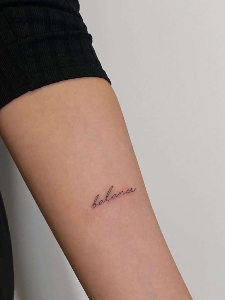 Minimalistyczny tatuaż fine line z napisem „balance”, zapisanym delikatnym, odręcznym pismem. Wykonany czarnym tuszem z czystą, precyzyjną kreską, ten subtelny tatuaż typograficzny symbolizuje wewnętrzną harmonię, spokój i osobistą równowagę. Wyrafinowany i dyskretny projekt umieszczony na przedramieniu, wykonany przez Yarę (@yaroslavaa.tattoo) w Fineline Tattoo Gallery dla Tattoo Kraków Kolektyw Artystów.